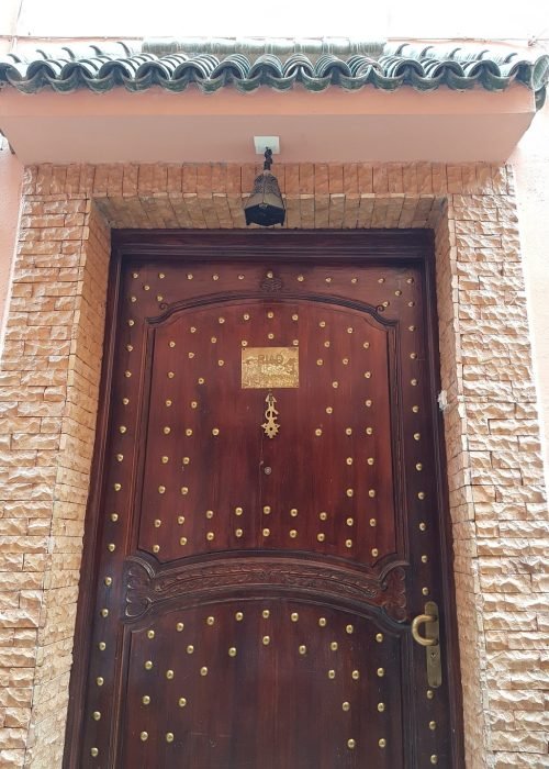 riad-s-front-door Charming bedroom in Riad Dar Benbrahim with decorative tiles and plush linens, blending heritage and comfort,